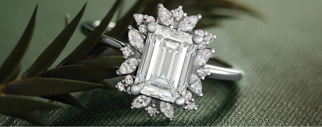 Diamond ring with emerald-cut center stone on a green fabric background